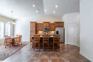 Kitchen with appliances with stainless steel finishes, brown cabinetry, backsplash, an island with sink, and vaulted ceiling