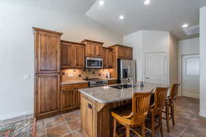 Kitchen with a kitchen bar, stainless steel appliances, light quartz counters, backsplash, and lofted ceiling