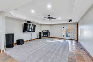 Unfurnished living room with a tray ceiling, stone tile flooring, a ceiling fan, a fireplace, and recessed lighting