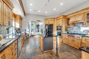Kitchen featuring backsplash, arched walkways, glass insert cabinets, appliances with stainless steel finishes, and a center island
