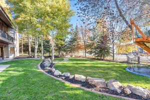 View of grassy yard featuring a trampoline, a patio area, and a balcony