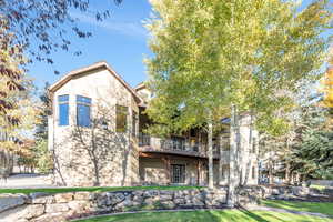 Back of house with stucco siding, a lawn, and a balcony