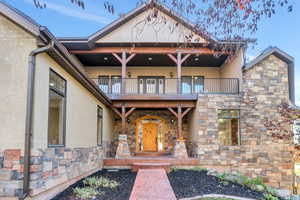 View of front of property with stone siding, stucco siding, covered porch, and a balcony