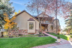 View of front facade with stone siding, stucco siding, a front yard, and a porch