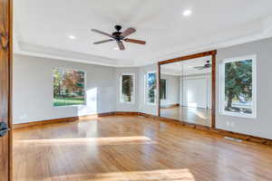 Spare room featuring a tray ceiling, light wood finished floors, healthy amount of natural light, ceiling fan, and recessed lighting