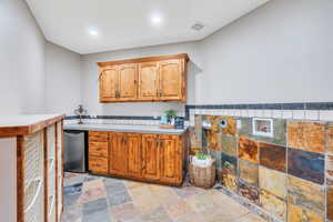 Kitchen featuring light countertops, stone tile flooring, tile walls, recessed lighting, and brown cabinets