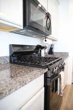 Kitchen with black appliances, white cabinets, and light stone countertops
