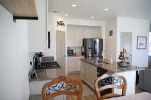 Kitchen featuring dark stone countertops, light wood-style floors, stainless steel refrigerator with ice dispenser, black range with gas stovetop, and recessed lighting