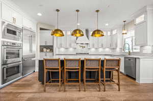 Kitchen with a breakfast bar, built in appliances, white cabinets, light stone countertops, and a textured ceiling