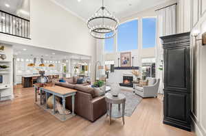 Living room with a glass covered fireplace, light wood-style flooring, crown molding, a chandelier, and recessed lighting