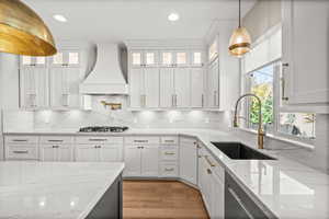 Kitchen with pendant lighting, white cabinets, light stone counters, custom range hood, and glass insert cabinets