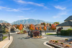 View of asphalt road with sidewalks, curbs, a residential view, a mountain view, and a gated entry