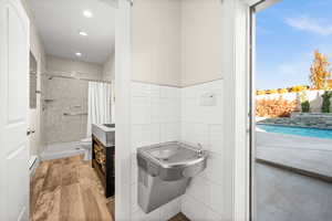 Bathroom featuring light wood-style flooring, healthy amount of natural light, tiled shower, a baseboard radiator, and tile walls