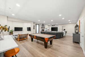 Basement Game room with recessed lighting, light wood-style flooring, billiards table, and a warm lit fireplace