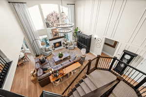 Living area with a warm lit fireplace, a decorative wall, a chandelier, wood finished floors, and a high ceiling