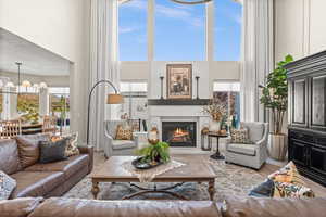 Living area with a high ceiling, healthy amount of natural light, a glass covered fireplace, wood finished floors, and a chandelier