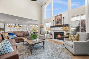 Living area with wood finished floors, a towering ceiling, a glass covered fireplace, crown molding, and a chandelier