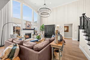 Living area with stairway, a glass covered fireplace, light wood finished floors, a high ceiling, and a chandelier
