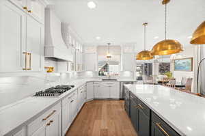 Kitchen with glass insert cabinets, light stone countertops, white cabinets, pendant lighting, and recessed lighting