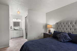 Bedroom featuring light colored carpet, a textured ceiling, and connected bathroom