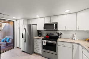 Kitchen featuring appliances with stainless steel finishes, white cabinetry, light stone counters, light tile patterned floors, and recessed lighting