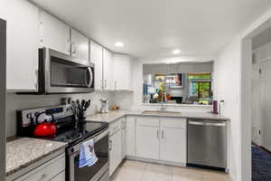 Kitchen with stainless steel appliances, white cabinets, light tile patterned floors, tasteful backsplash, and light stone countertops