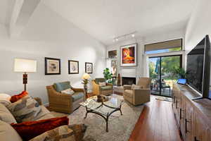 Living room featuring hardwood / wood-style flooring, a fireplace, high vaulted ceiling, a textured ceiling, and rail lighting