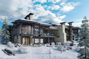 Snow covered back of property with a balcony, stone siding, a chimney, and a patio