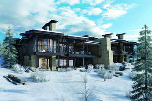 Snow covered rear of property with a balcony, stone siding, and a patio