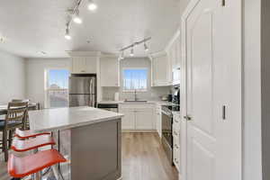Kitchen with a kitchen island, stainless steel appliances, white cabinets, a textured ceiling, and a kitchen bar