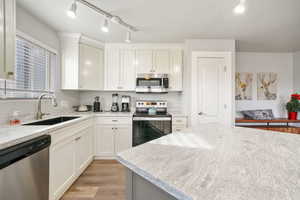 Kitchen with appliances with stainless steel finishes, light wood-type flooring, track lighting, and white cabinets