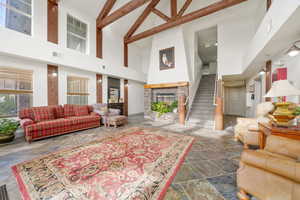 Living room featuring high vaulted ceiling, stairs, beamed ceiling, stone tile flooring, and a fireplace