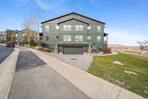 View of front of property with board and batten siding, asphalt driveway, a front lawn, and an attached garage