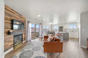 Living area with a textured ceiling, wood walls, light wood-style flooring, a large fireplace, and rail lighting