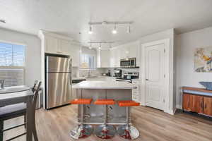 Kitchen with appliances with stainless steel finishes, a center island, a kitchen breakfast bar, light wood finished floors, and a textured ceiling