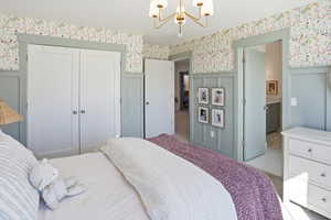 Carpeted bedroom with a chandelier, wallpapered walls, a closet, a wainscoted wall, and ensuite bathroom