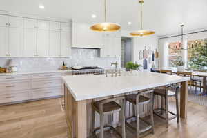 Kitchen with backsplash, white cabinets, light wood-type flooring, decorative light fixtures, and recessed lighting