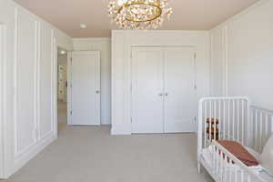 Carpeted bedroom featuring a crib, a chandelier, and a closet