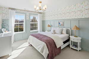 Bedroom with wallpapered walls, carpet flooring, a decorative wall, a chandelier, and wainscoting