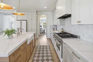 Kitchen featuring premium appliances, white cabinetry, recessed lighting, light stone countertops, and custom range hood