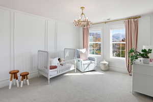Bedroom featuring a decorative wall, carpet flooring, a chandelier, and a nursery area