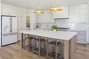 Kitchen featuring high end fridge, backsplash, decorative light fixtures, light wood-style flooring, and an island with sink