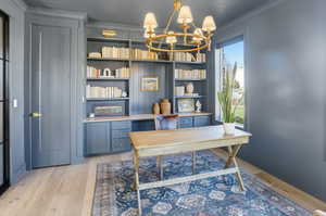 Home office featuring light wood finished floors, ornamental molding, and a chandelier