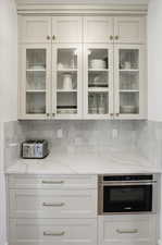 Kitchen featuring light stone counters, decorative backsplash, and white cabinets