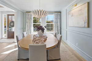 Dining space featuring a chandelier, wood finished floors, a decorative wall, plenty of natural light, and crown molding