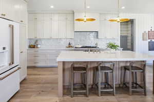 Kitchen featuring high end white refrigerator, decorative backsplash, light stone countertops, light wood-type flooring, and pendant lighting