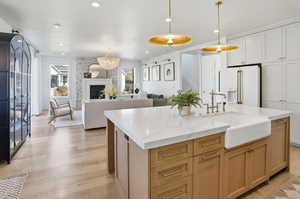 Kitchen with open floor plan, hanging light fixtures, light wood finished floors, white fridge with ice dispenser, and light stone counters