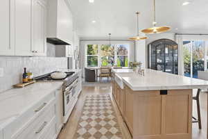 Kitchen featuring double oven range, a kitchen breakfast bar, decorative light fixtures, light stone counters, and backsplash