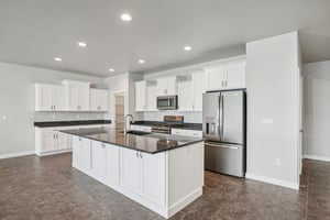 Kitchen featuring appliances with stainless steel finishes, white cabinetry, dark countertops, a center island with sink, and recessed lighting