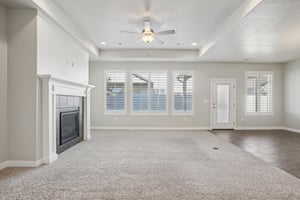 Unfurnished living room with healthy amount of natural light, a fireplace, ceiling fan, and a raised ceiling
